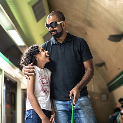Blind parent and child walking together through a subway station.