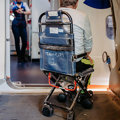 Passenger seated in an onboard wheelchair being assisted aboard an aircraft.